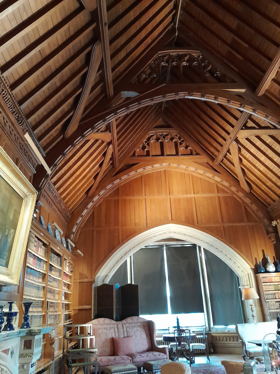 Victorian library interior with vaulted wooden ceiling, timber beams, bookshelves, and armchairs