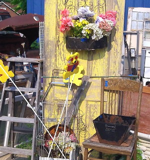 Clutered junk shop display with flower baskets, yellow toy, and vintage furniture against yellow wall