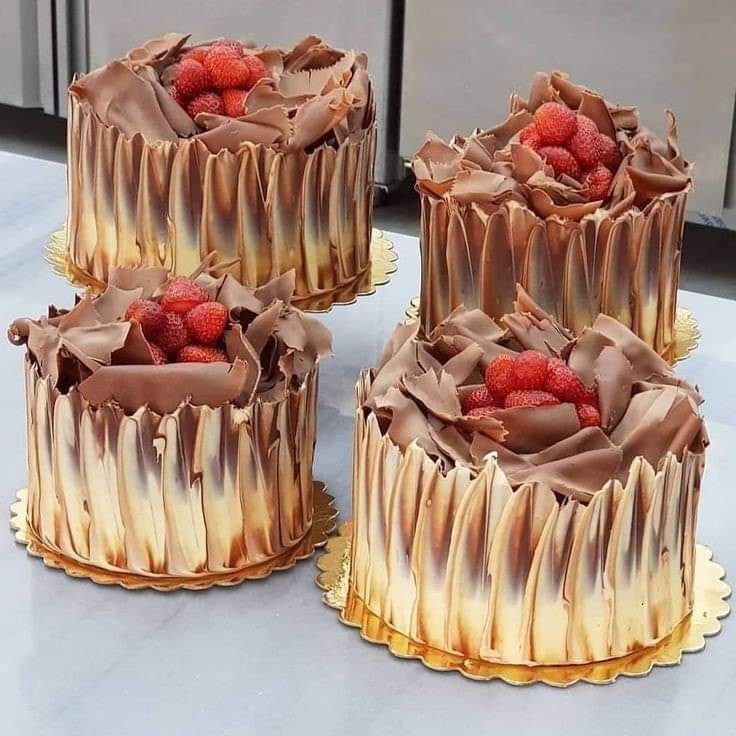 Four small round cakes with chocolate drip icing, chocolate ruffles, and strawberries on top