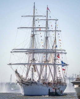White tall sailing ship docked on calm water with multiple masts and rigging
