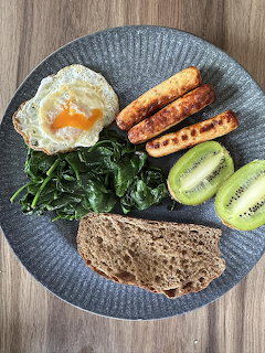 Overhead view of a healthy breakfast plate with egg, greens, cheese, bread, and sliced kiwi on wooden table
