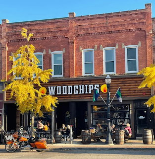 Brick restaurant storefront with Woodchips sign, yellow autumn trees, patio seating, and motorcycles