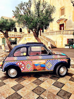 Colorful vintage Fiat 500 with decorative patchwork paint in a sunny Mediterranean square