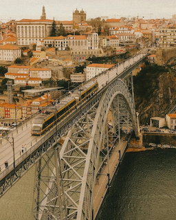 Double-deck metal arch bridge over river with historic European city buildings on hillside in warm afternoon light
