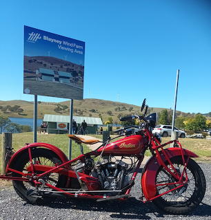 Red vintage Indian motorcycle parked by lake with mountains and blue sky