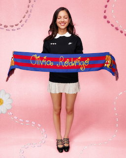 Smiling young woman holding a blue and red striped scarf above her head against a pink backdrop