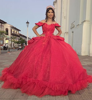 Woman wearing a large sparkly red quinceañera ball gown and tiara posing on a colonial street