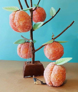 Miniature peach tree sculpture with sugared peaches, small ladder, and tiny figure against turquoise backdrop