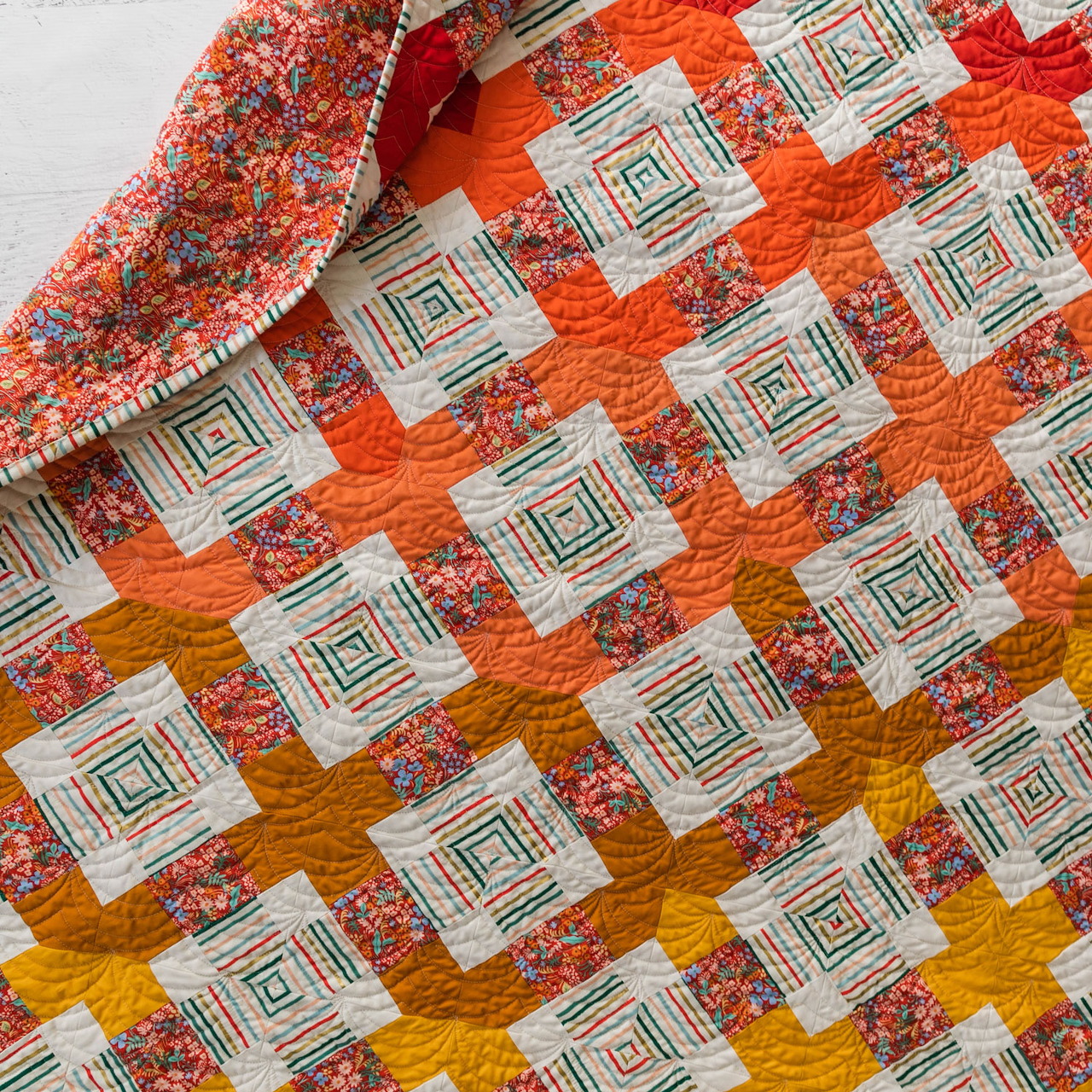 Geometric patchwork quilt with orange and yellow log cabin squares arranged in diagonal pattern with floral accents