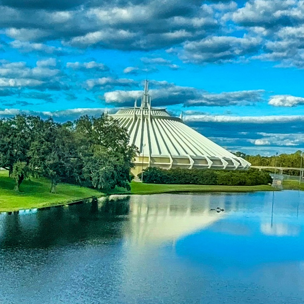 Space Mountain white pyramid structure reflected in lake with blue cloudy sky