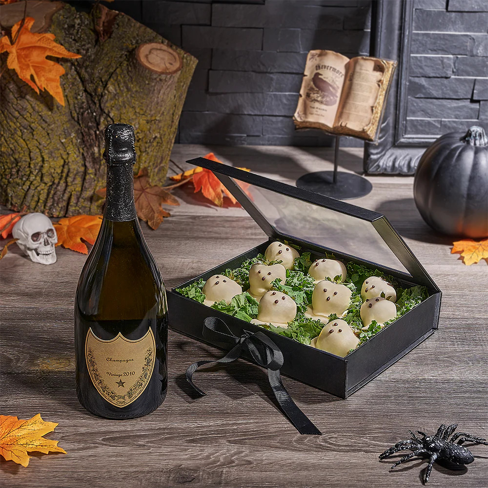 Champagne bottle next to open box of ghost-shaped white chocolates with Halloween decorations on wooden table