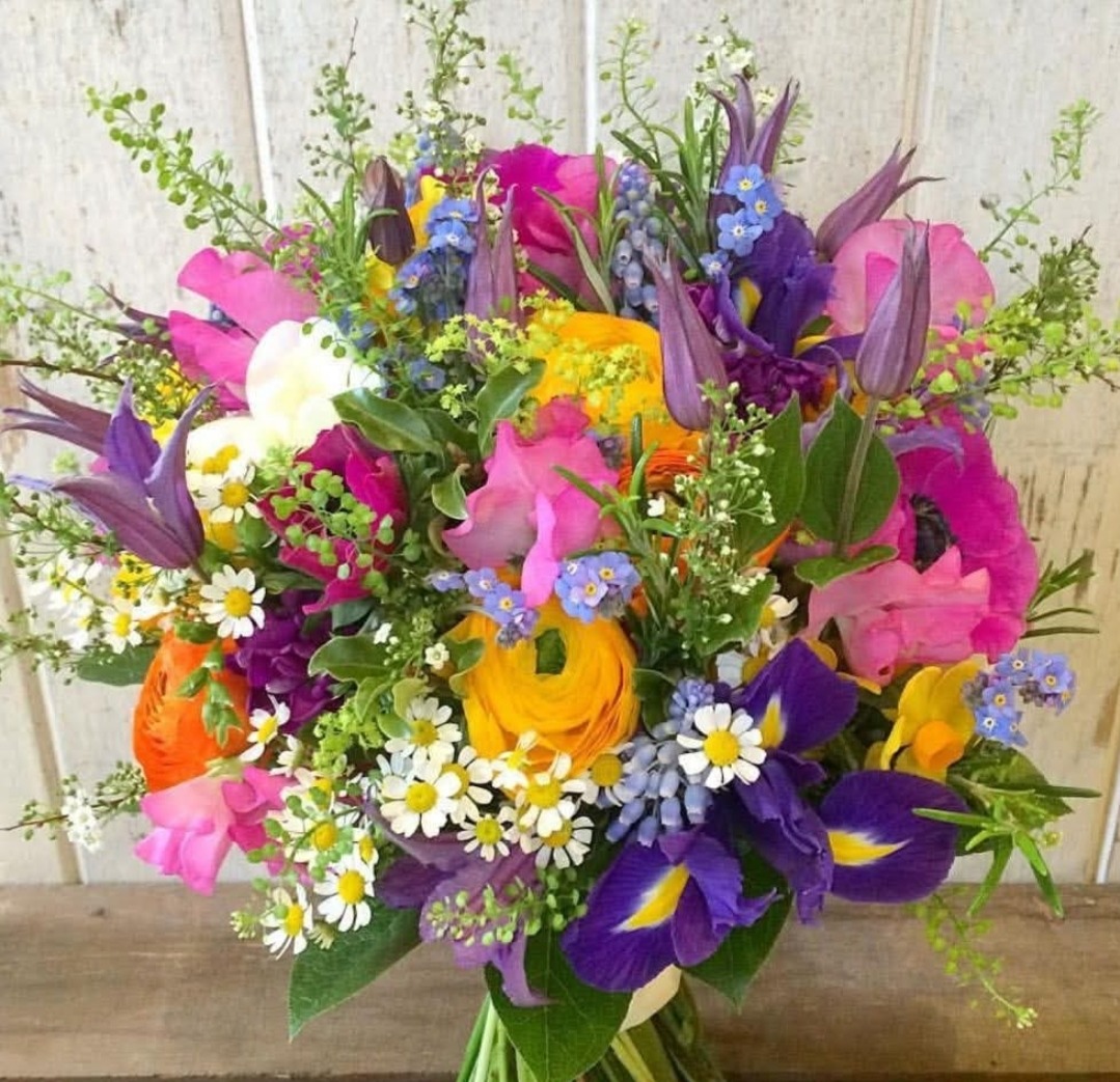 Colorful bouquet of spring flowers including tulips, irises, daisies and ranunculus on wood background