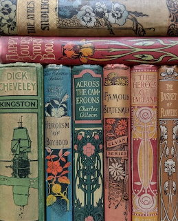Stack of ornate antique book spines with decorative gold patterns and colorful covers in red, green, and coral