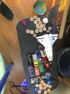 Toy cars, space shuttle model, and wooden checkers pieces scattered on a dark board