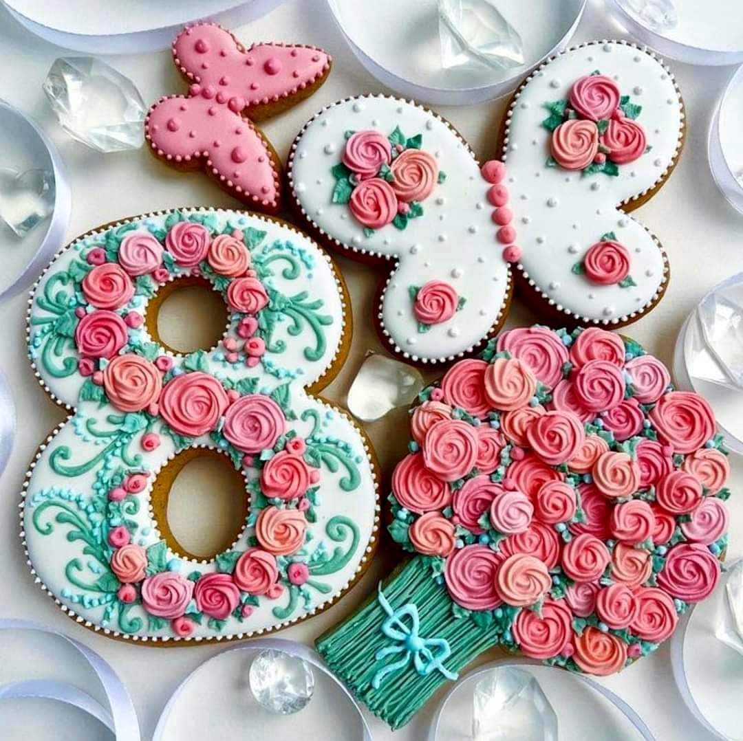 Ornate frosted cookies with pink roses and teal trim on white fabric