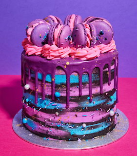 Purple drip cake with macarons and pink frosting on a pink table