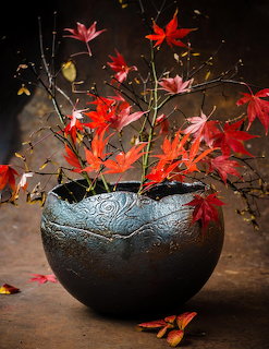 Red autumn leaves in decorative black ceramic bowl on dark surface