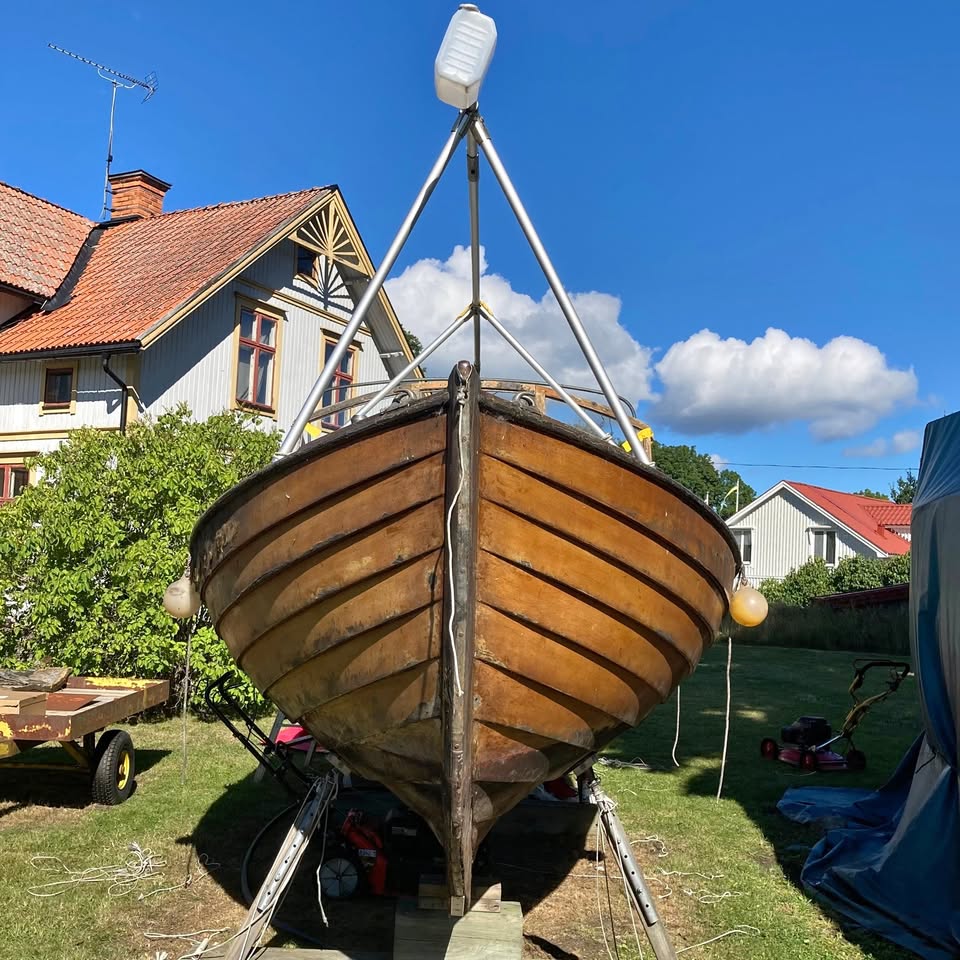 Wooden boat on supports in a grassy yard beside houses under a blue sky
