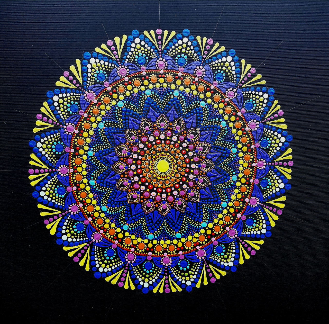 Circular mandala with intricate dot-painted patterns in vibrant blues, yellows, oranges, and reds on dark blue background