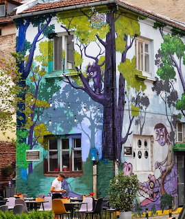 Vibrant street art mural on building exterior with painted tree, houses and whimsical figures in Plovdiv Bulgaria