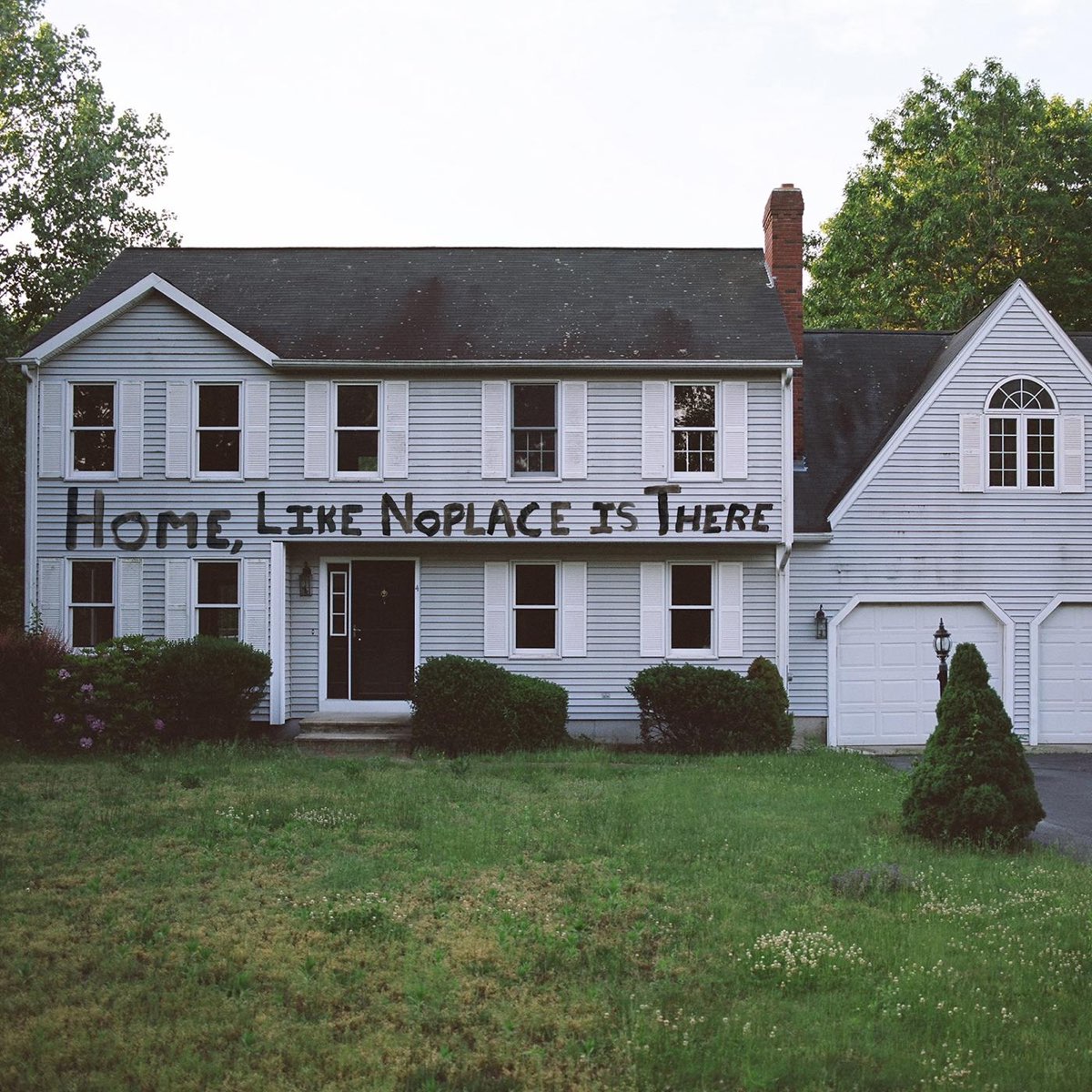 White two-story house with lawn and handwritten text across the front