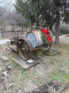 Holiday wreath with red bow decorating an old drum on a wheeled cart in a farm yard