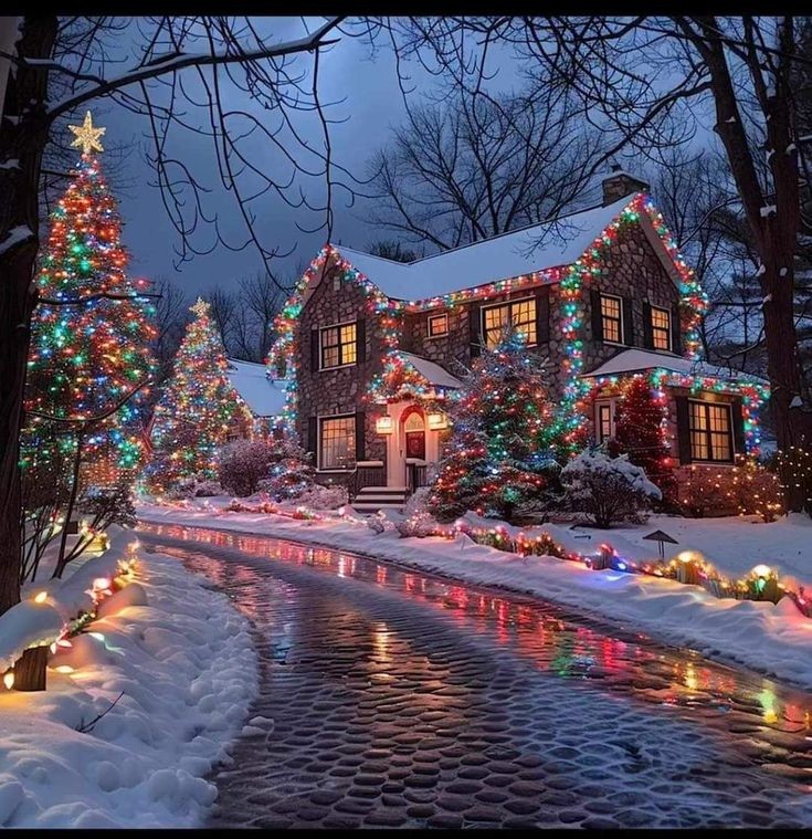 Festive house covered in Christmas lights and snow with decorated trees and lit pathway at dusk