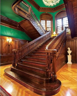 Grand wooden staircase in a historic interior with green walls, chandelier, and arched windows