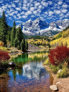 Maroon Bells mountains with snow peaks reflected in a clear lake surrounded by fall foliage in Colorado
