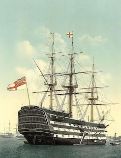 Historic British tall ship with masts and rigging anchored in a harbor, British flag flying