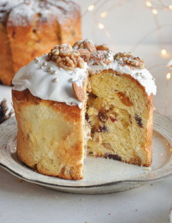 Sliced panettone cake with white icing and candied fruit on a white plate