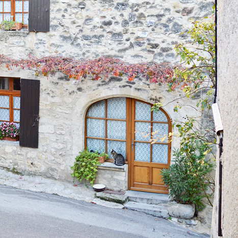 Stone building facade with arched wooden door and flower boxes in Cucuron France