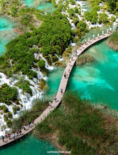 Aerial view of wooden boardwalk over turquoise water at Plitvice Lakes with waterfalls and green foliage