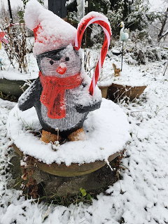 Snow-covered decorative penguin statue with red scarf and candy cane in a winter garden