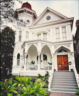 White Victorian house with arched porch, wooden doors, tower, and green landscaping