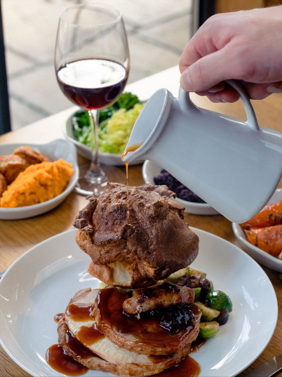 Plated roast beef with vegetables, wine glass, and golden sides on white plate