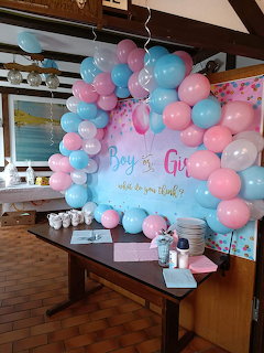 Gender reveal party with pink and blue balloon arch behind a table with cups and decorations