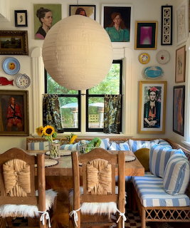 Eclectic dining nook with wooden chairs, blue striped cushions, paper lantern, sunflowers, and gallery wall