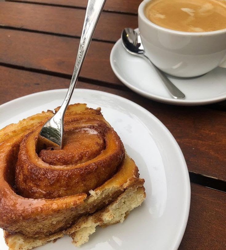 Cup of coffee and a cinnamon roll on white plates on a wooden table