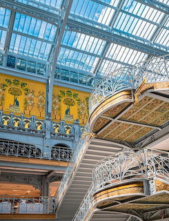 Ornate Art Nouveau interior with glass ceiling, decorative ironwork, and grand staircase in La Samaritaine Paris