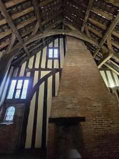 Interior of medieval hall with brick chimney breast, timber frame walls, and exposed wooden roof beams