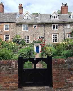 Stone cottage with rose garden and black entrance gate under cloudy sky