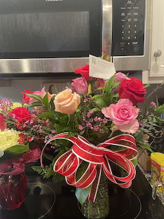 Colorful bouquet of roses with red and white ribbon in a vase on a kitchen counter