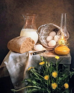 Rustic still life with bread, milk, eggs, oil lamp, and dandelions on a wooden table