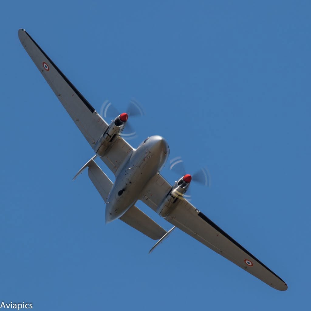 Vintage twin-engine propeller airplane seen from below in a clear blue sky