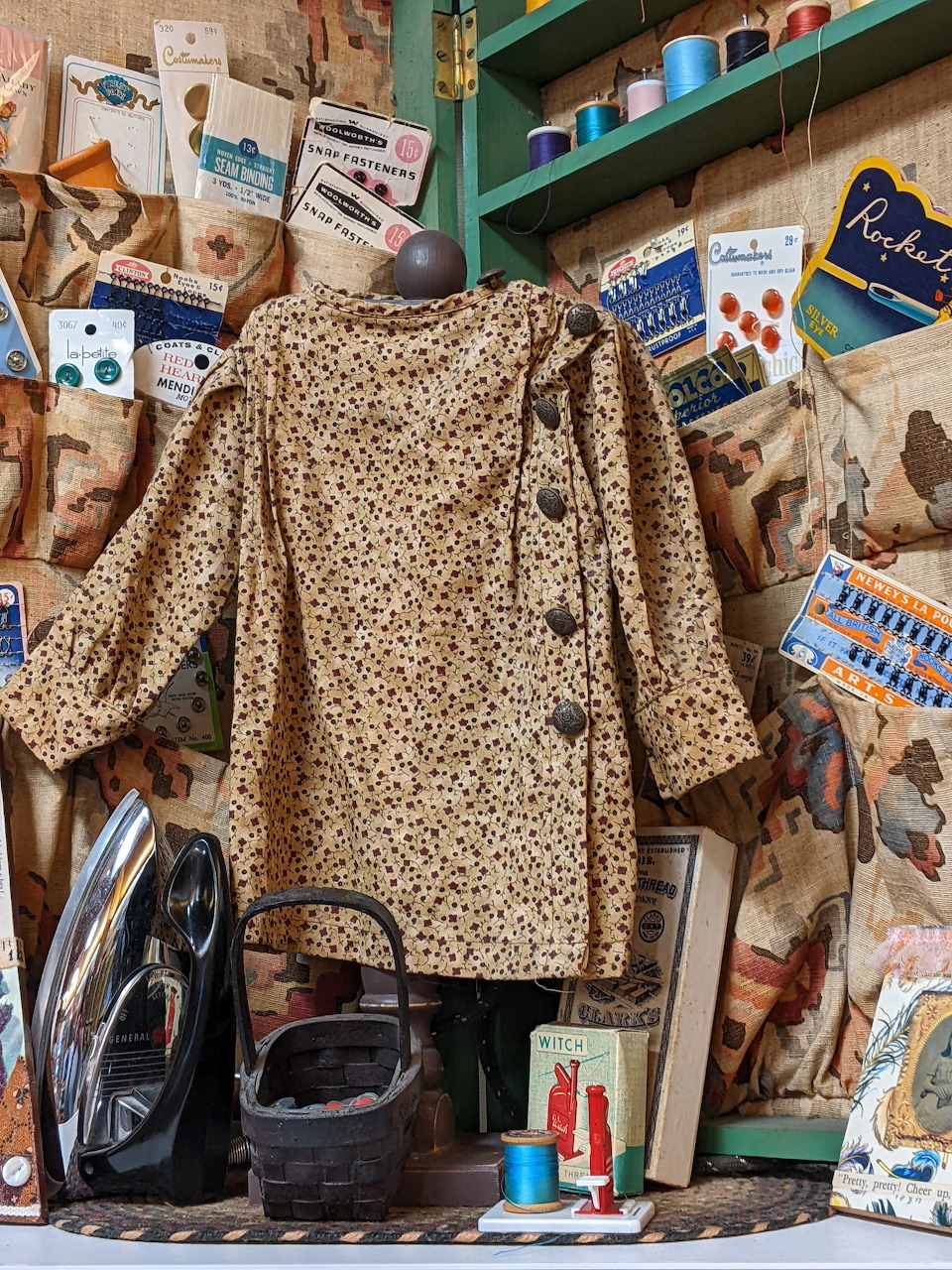 Vintage sewing display with old blouse on mannequin, antique irons, thread spools, and sewing notions