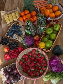 Assorted fruits and vegetables on a wooden table with strawberries, apples, tomatoes, corn, and cabbages