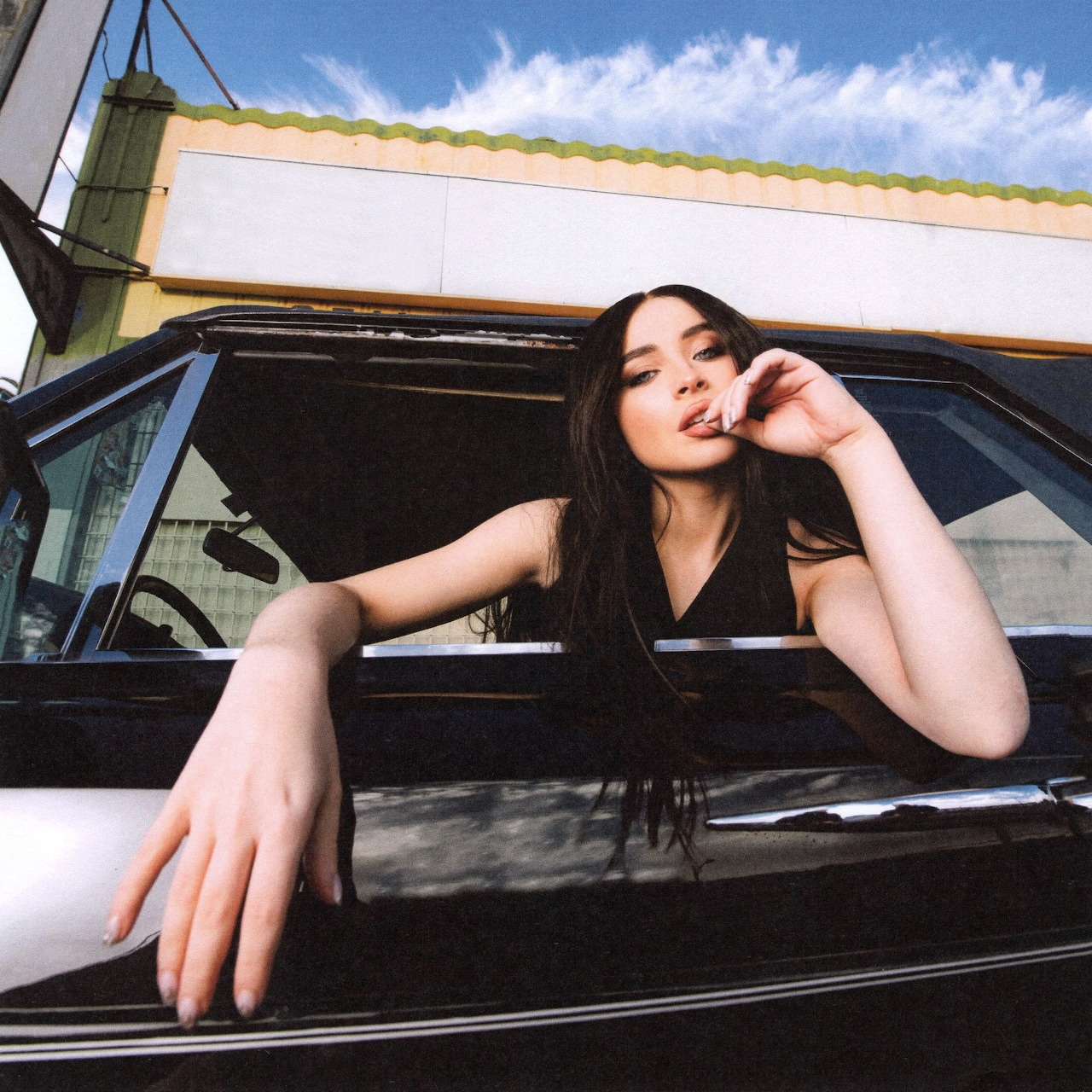 Woman with long dark hair leaning out of black car window against blue sky