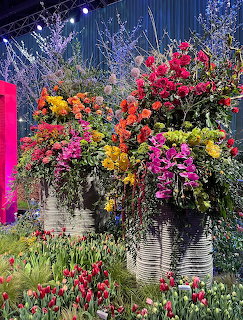 Large textured planters overflowing with colorful flowers including tulips and mixed blooms at a flower show