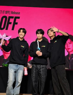 Three young men posing on an indoor stage with a bright pink backdrop